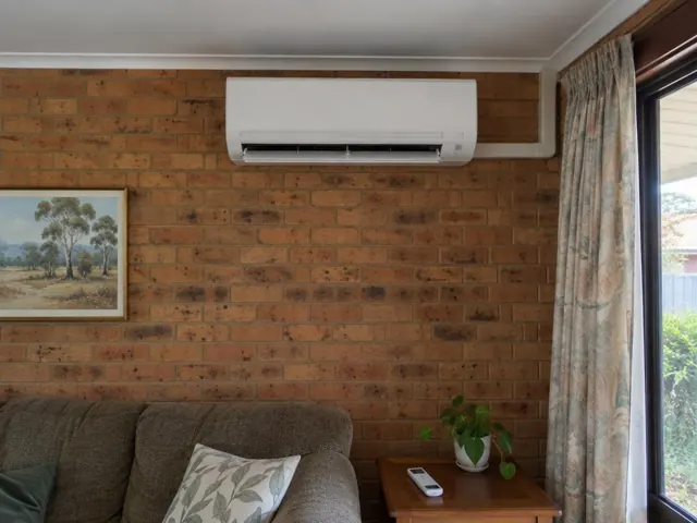 Wall-mounted split system on a brick living room wall above a sofa, with curtains and a window in Happy Valley